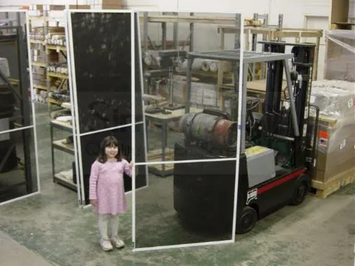 A child standing beside a Simplicity panel far taller than she is, in the workshop