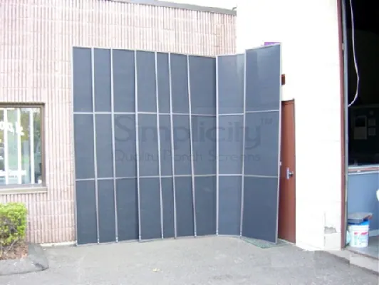 Large finished screen panels stacked against a brick wall outside the workshop
