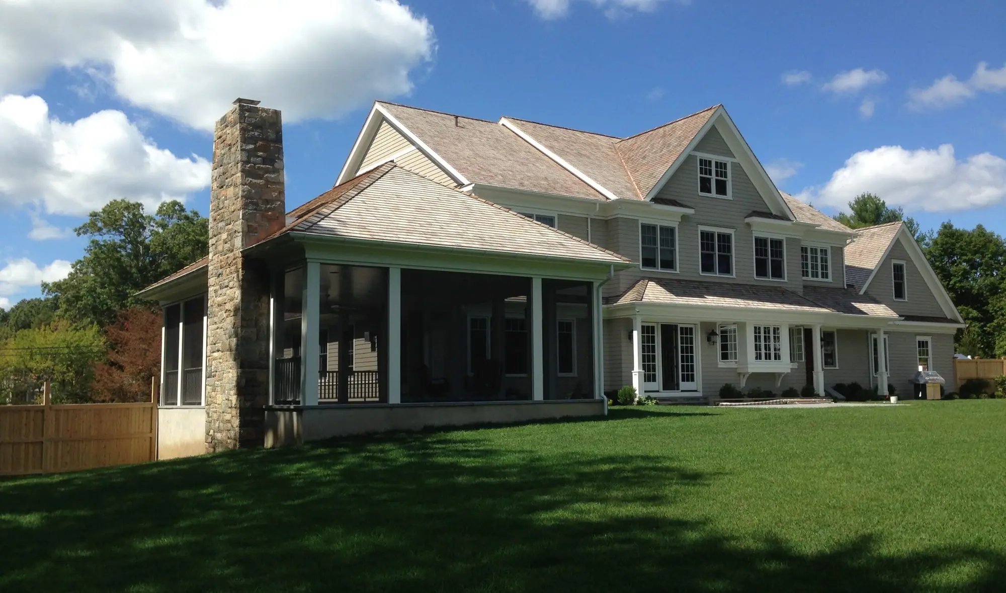 A large clapboard house with a stone chimney and a screened porch under the main roof