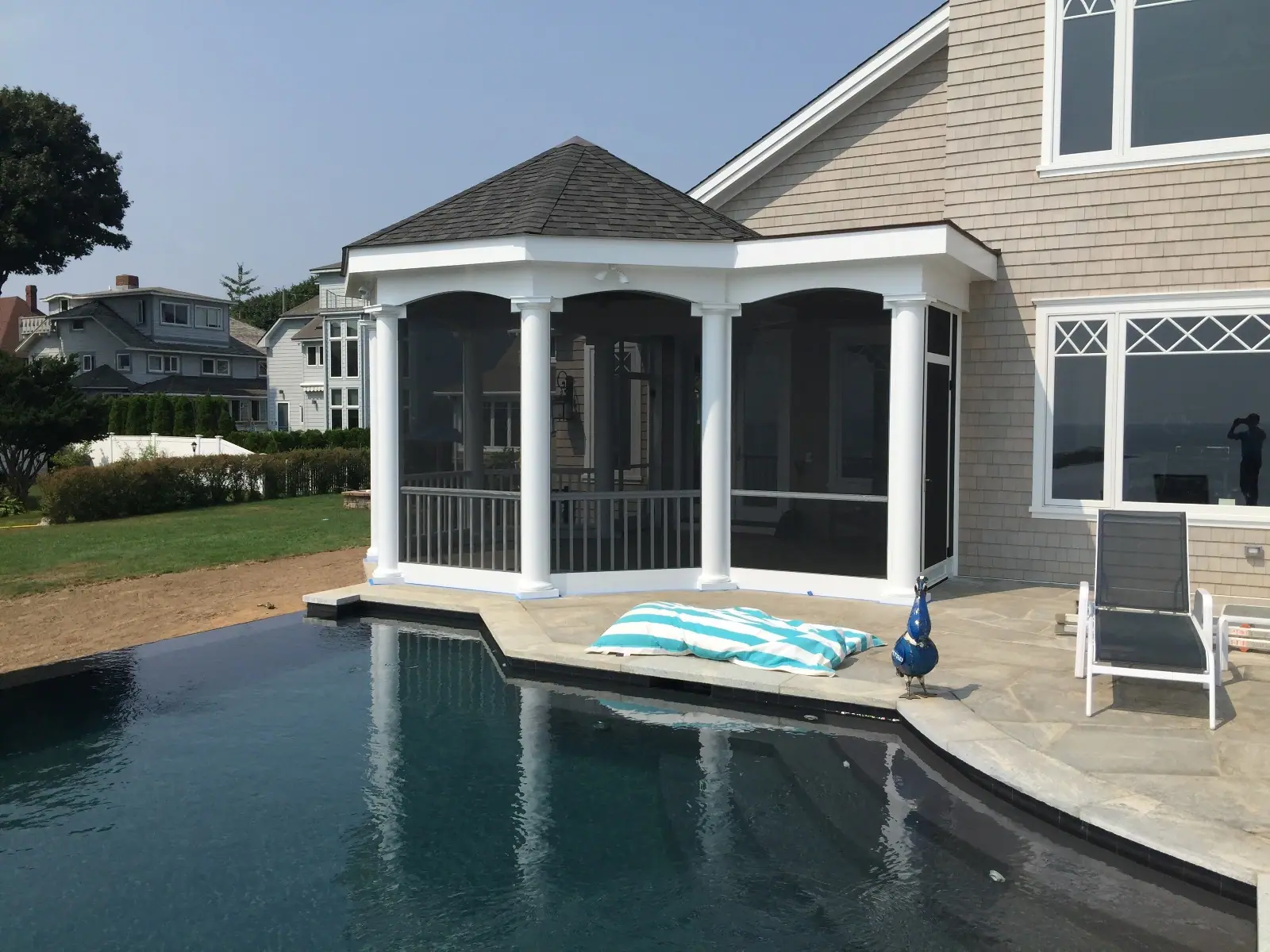A screened gazebo beside a swimming pool, with towels and a lounger on the paving