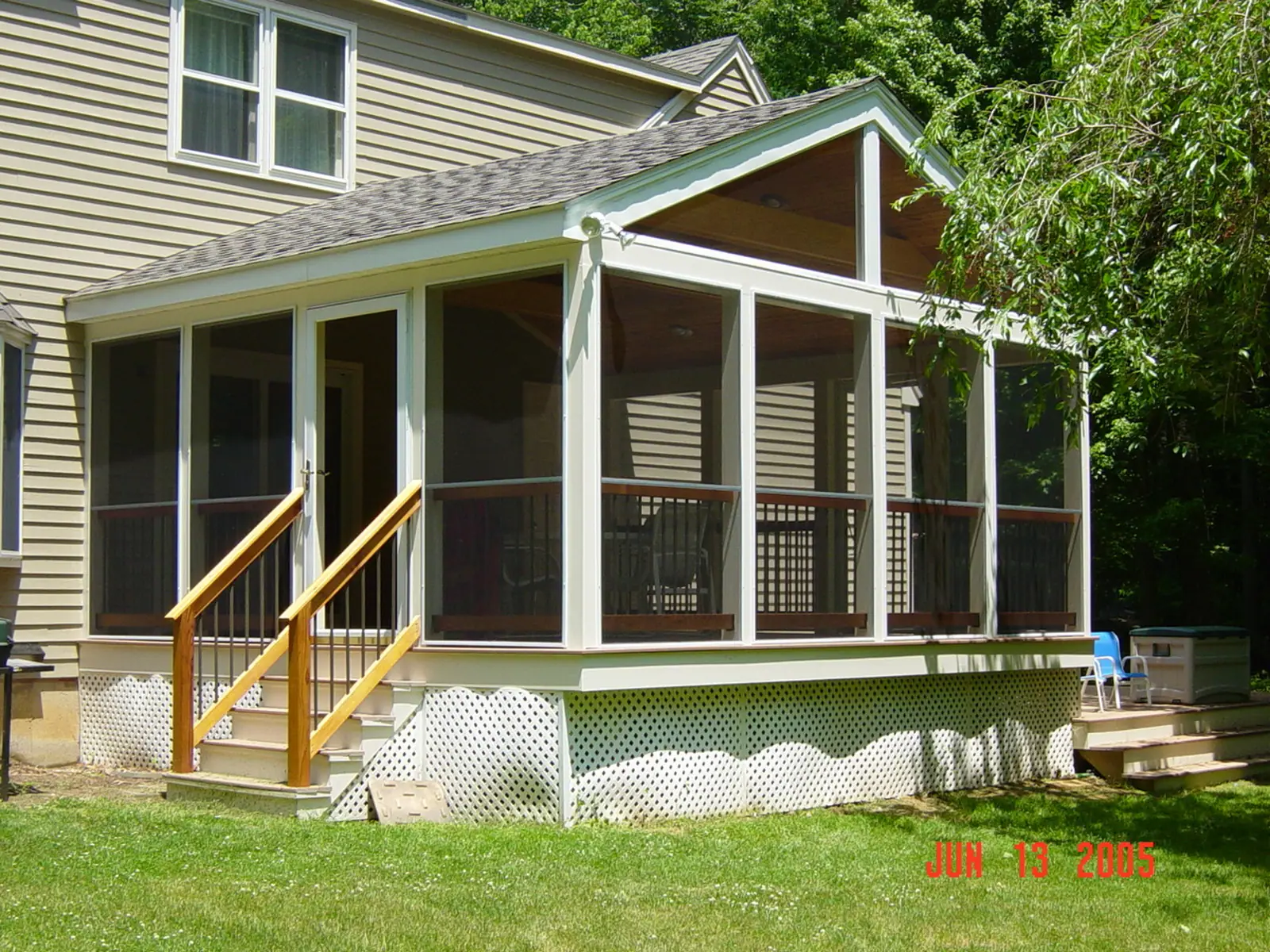 A tan clapboard house with a screened porch addition and timber steps down to the lawn