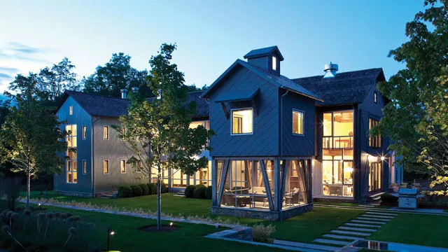 A modern blue-clad house lit at dusk, its lower level screened and open to the garden