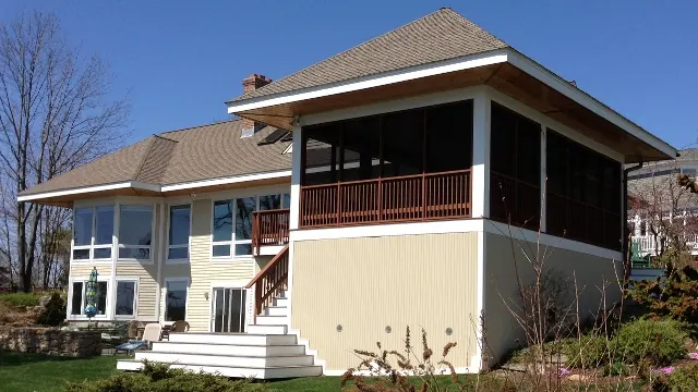 A screened porch enclosure on a hillside home under a clear blue sky