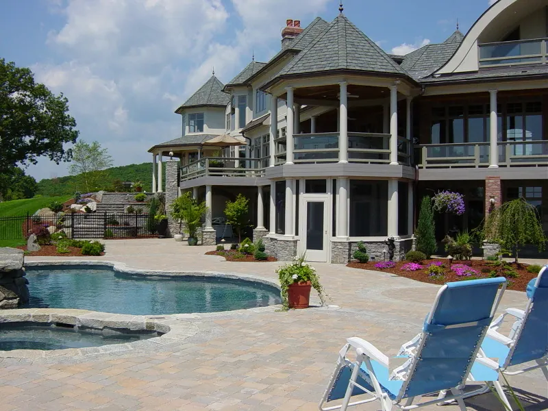 A large shingle-style house with a turret and screened verandah, seen across a curved swimming pool