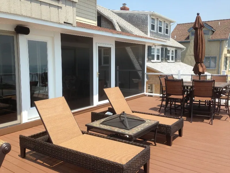 A timber deck with loungers and a dining set in front of a screened porch