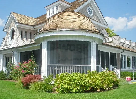 A shingle-style house with a turret and a screened wraparound porch