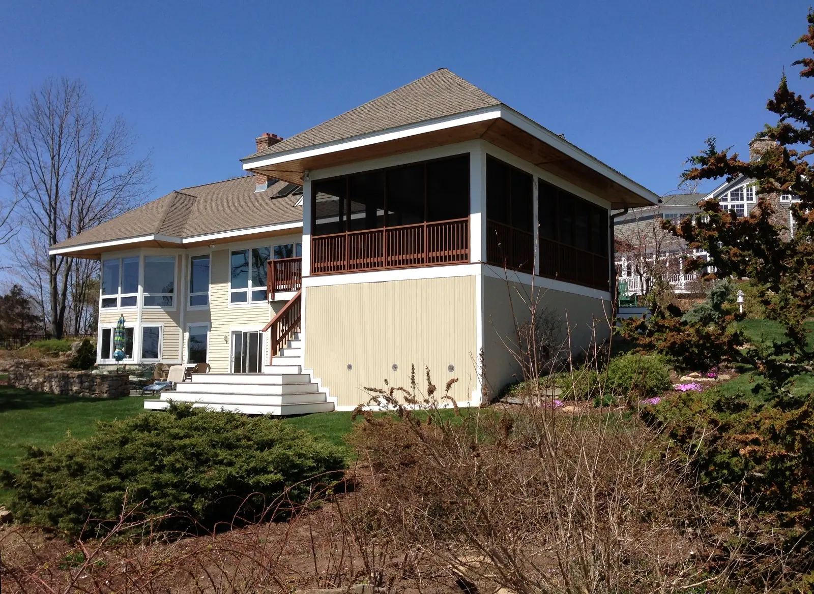 A hillside home with a screened porch enclosure above a walk-out lower level